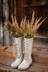autumn bouquet in rubber boots on the background of old wooden doors and the village threshold.