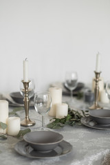 Fototapeta na wymiar Table setting: gray dishes, white candles, candlesticks, glass goblets, sprigs of eucalyptus on a wooden table 