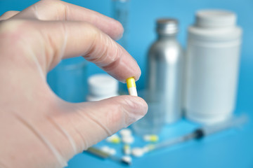 A hand in gloves holds a medical capsule with on the background of medical cans, pills on a blue background.