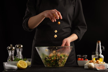 The chef cooks a salad and sprinkles crackers. Freeze in motion. Seafood and cooking healthy food on a black background. Cooking and gastronomy, a lot of recipe