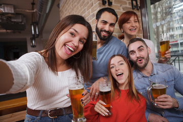 Charming excited woman taking selfies with her friends at beer pub. Friends enjoying drinking beer together
