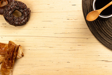 Chocolate donuts and food supplements like spoon and coffee on light wooden background from an overhead shot. Breakfast concept.