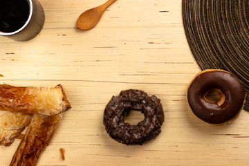 Chocolate donuts and food supplements like spoon and coffee on light wooden background from an overhead shot. Breakfast concept.