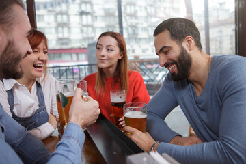Happy young people enjoying relaxing together at beer pub. Group of friends laughing over a joke while drinking beer