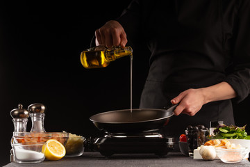 The chef prepares a sauce for salad, pours oil for cameralization of shrimp. Freezing in motion, preparing healthy and wholesome food. On a black background for design.