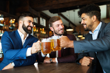 Cheerful old friends having fun and drinking beer at bar counter in pub.