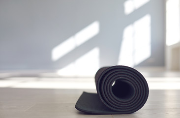 Black yoga mat on the floor of a bright sunny studio.