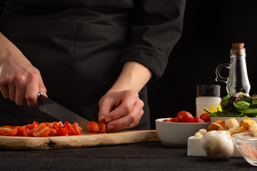 Chef slices cherry tomatoes closeup for cooking sauce. Seafood and oriental recipes.
