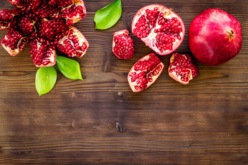 Ripe pomegranate fruit near leaf on dark wooden background top-down copy space