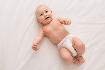 baby boy 5 months old smiling in diapers lying on the bed, top view