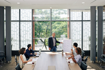 Mature entrepreneur talking to employees at meeting and explaining new marketing strategy