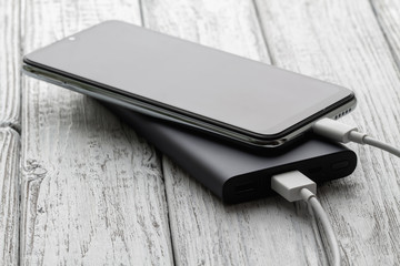 The smartphone is charging from external powerbank with cable on a gray wooden background. Closeup, selective focus