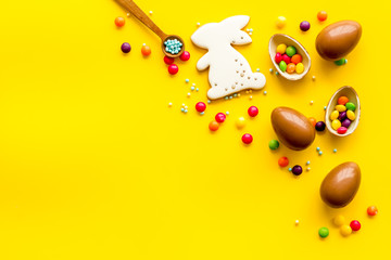 Sweet Easter symbols - chocolate eggs and bunny gingerbread - on yellow background top-down frame copy space