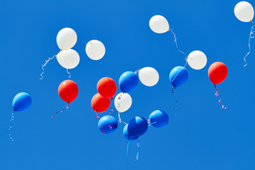 Multicolored helium balloons flying up in the blue sky