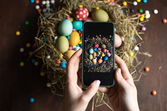 Woman making picture on mobile phone of  Easter eggs in nest