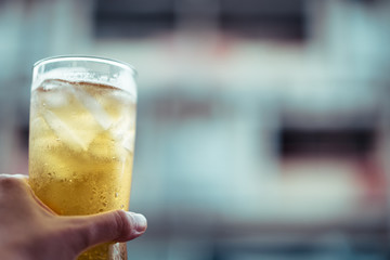glass of cold beer with ice holding by left hand, cheers moment, vintage tone