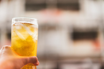 glass of cold beer with ice holding by left hand, cheers moment, vintage tone