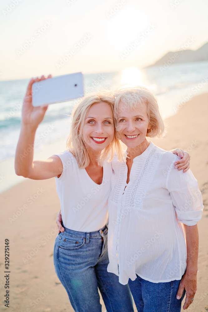 Wall mural outdoor portrait of smiling happy caucasian senior mother with her adult daughter taking selfie on s