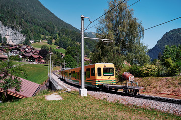 Beautiful mountains landscape. Yellow-green train running through the Swiss Grindelwald Village,...