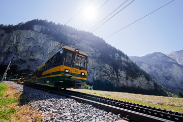 Obraz premium Beautiful mountains landscape. Yellow-green train running through the Swiss Grindelwald Village, Switzerland.