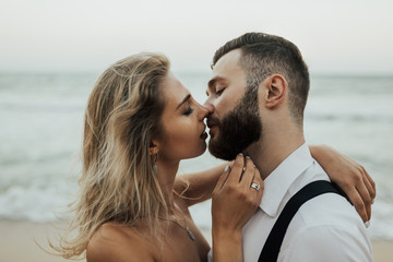 Close up portrait of a sensual beautiful married couple at the beach. Profile of newlyweds with closed eyes. Emotional moment on their wedding day. 