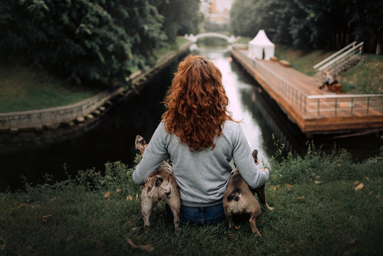 Woman With Red Curly Hair Sitting Outdoors With Two Dogs, Rear View