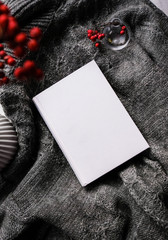Winter autumn mock up with white book cover. Greetings card new year book mockup with red rowan berries over gray wool plaid. White book cover winter cozy mock-up.Warm festive rowan tree backdrop.
