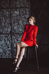 Beautiful woman lady in a red dress sits sadly on a bar stool in the loft style. Soft selective focus. Beauty, fashion.