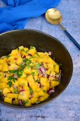 Fresh homemade mango salsa in a bowl on blue background