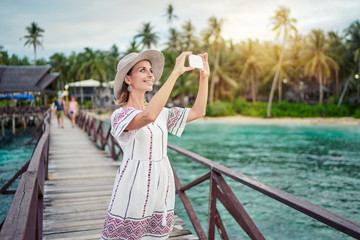 Vacation and technology. Outdoor portrait of pretty young woman taking photo with her smartphone on tropical beach.