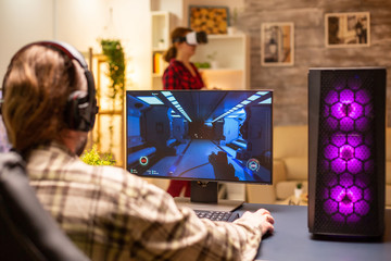 Back view of professional video gamer playing on powerful PC late at night in the living room