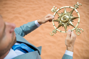 Lost businessman holding a traditional old-fashioned compass rose outdoors in the desert