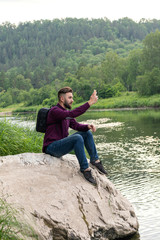 Fototapeta na wymiar young man using cellphone, bearded hipster traveler doing selfie. Vacation, tourism, internet, technology concept