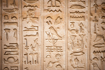 Full frame close-up of series of Egyptian hieroglyphs carved into rough stone temple wall in Luxor, Egypt