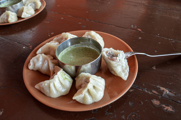 Indian kitchen. Tasty chicken momos with spicy kenza sauce on a wooden vintage background.