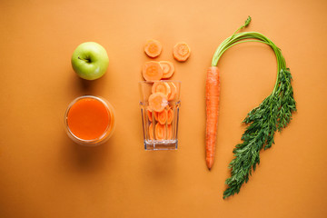 Flat lay composition with fresh carrot juice, apple and fresh carrots on a brown background.