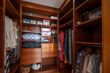 Modern wooden wardrobe with clothes hanging on rail in walk in closet.