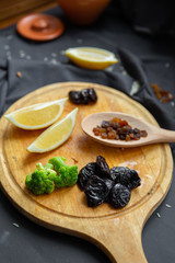 Ingredients for cooking. Products on a round wooden board: lemon slices, prunes, broccoli and dried grapes (raisins) in a wooden spoon. 