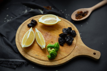 Ingredients for cooking. Products on a round wooden board: lemon slices, prunes, broccoli and dried grapes (raisins) in a wooden spoon. 