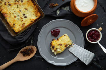 Cottage cheese casserole with raisins on a gray plate, poured sour cream on top. Flat lay, view from above. 