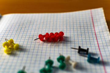 Colored small office buttons with different convenient protective hats, modern office details scattered on notebook leaves in a check