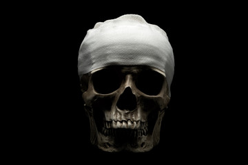 Human skull with dramatic lightning and bandages on the head is isolated on a black background.