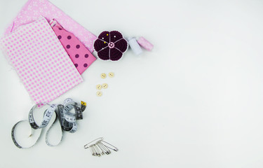 Pink fabric, spools of thread, scissors, ribbon, wooden buttons, pins. The concept of a hobby, creativity, sewing.