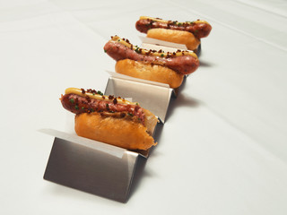 Three small hotdogs in bread and metal stand on white cloth