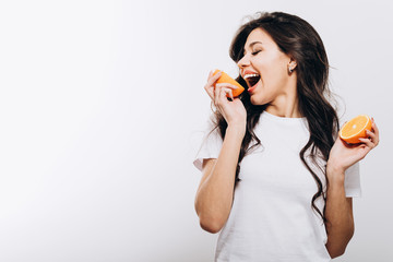 Playful cute brunette girl playing fool with halves of orange isolated white background copyspace