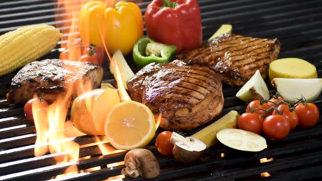 Footage of assorted grilled meat with vegetable on the flaming grill .