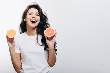 Smiling young brunette beauty posing with a half of orange and a half of grapefruit isolated white...
