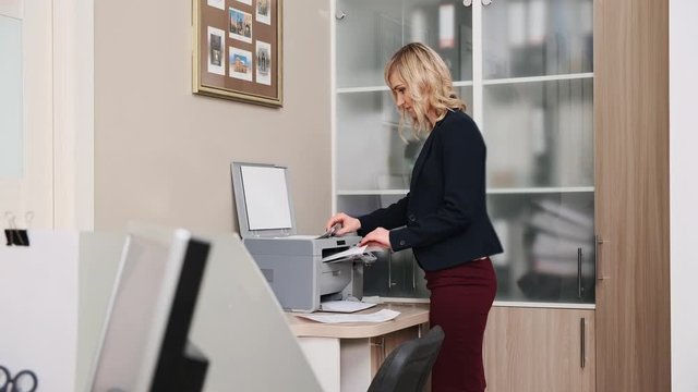 A young woman in a jacket, an office worker prints documents on a copy machine. Paperwork.
