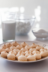Merinque cookies in white plate. Glass of milk, white bowls background.High key food photography.