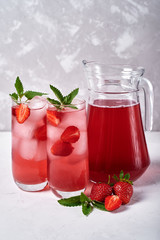 Fresh strawberry lemonade with ice and mint in glasses and jug on white table, copy space. Cold summer drink. Sparkling glass with berry cocktail